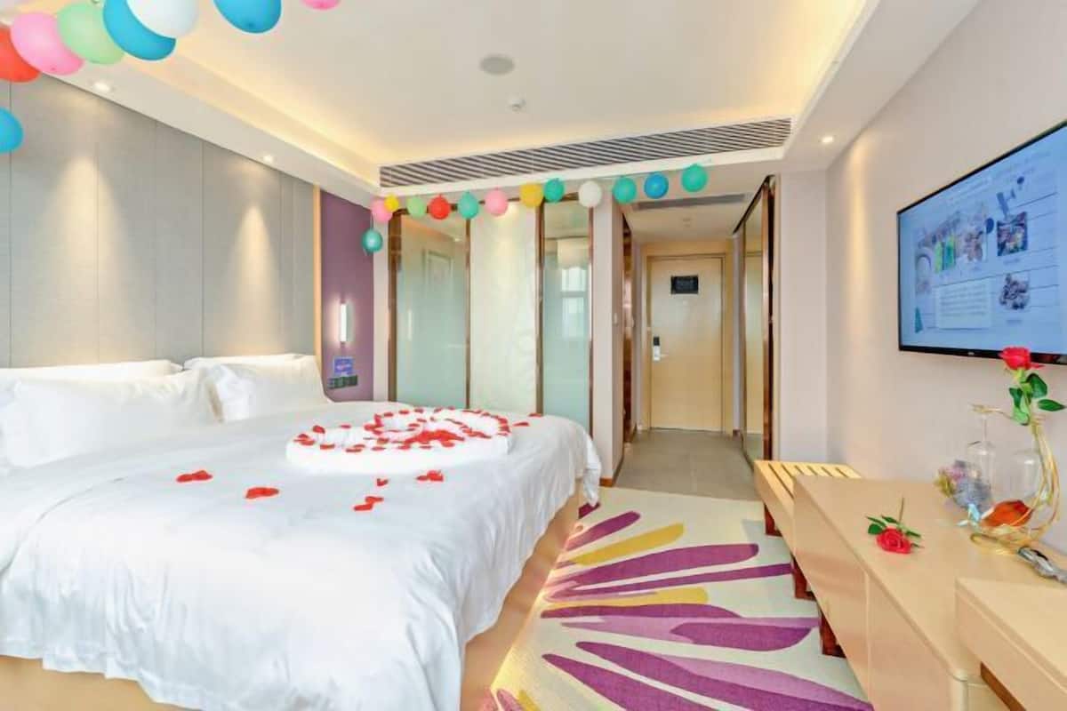 A hotel room with a bed, a desk, a television, and a wall-mounted screen.