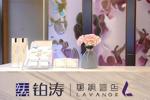 A reception desk with a vase of flowers, a framed picture, and a sign with text. - Lavande Hotel (Guangzhou Jiahe Wanggang Metro Station) (Guangzhou)