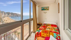 Een balkon kamer met een bed, een schilderij en uitzicht op het strand en de stad.