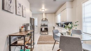 A modern kitchen with white cabinets, stainless steel appliances, and a dining area with grey chairs and a glass table. - 15% Summer Discount~ Entire Home ~ Full Kitchen ~ Large Fenced Backyard (Oklahoma City)