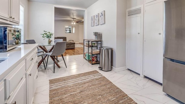 A modern kitchen with white cabinetry, a stainless steel refrigerator, and a dining area with a table and chairs. - 15% Summer Discount~ Entire Home ~ Full Kitchen ~ Large Fenced Backyard (Oklahoma City)