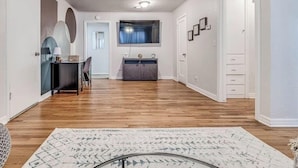 A hallway with a wooden floor, a desk with a chair, a cabinet, and a television on the wall. - 15% Summer Discount~ Entire Home ~ Full Kitchen ~ Large Fenced Backyard (Oklahoma City)