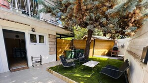 En trädgård med en grillplats, ett träd och en uteplats med stolar.