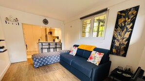 Ett kompakt bostadsutrymme med en soffa, ett litet bord, en liten köksdel och ett fönster med utsikt.