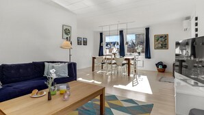 A modern living room with a sofa, coffee table, and dining area. There are framed pictures on the walls and a large window with curtains. - 2 bedroom stunning home in Svaneke (Svaneke)