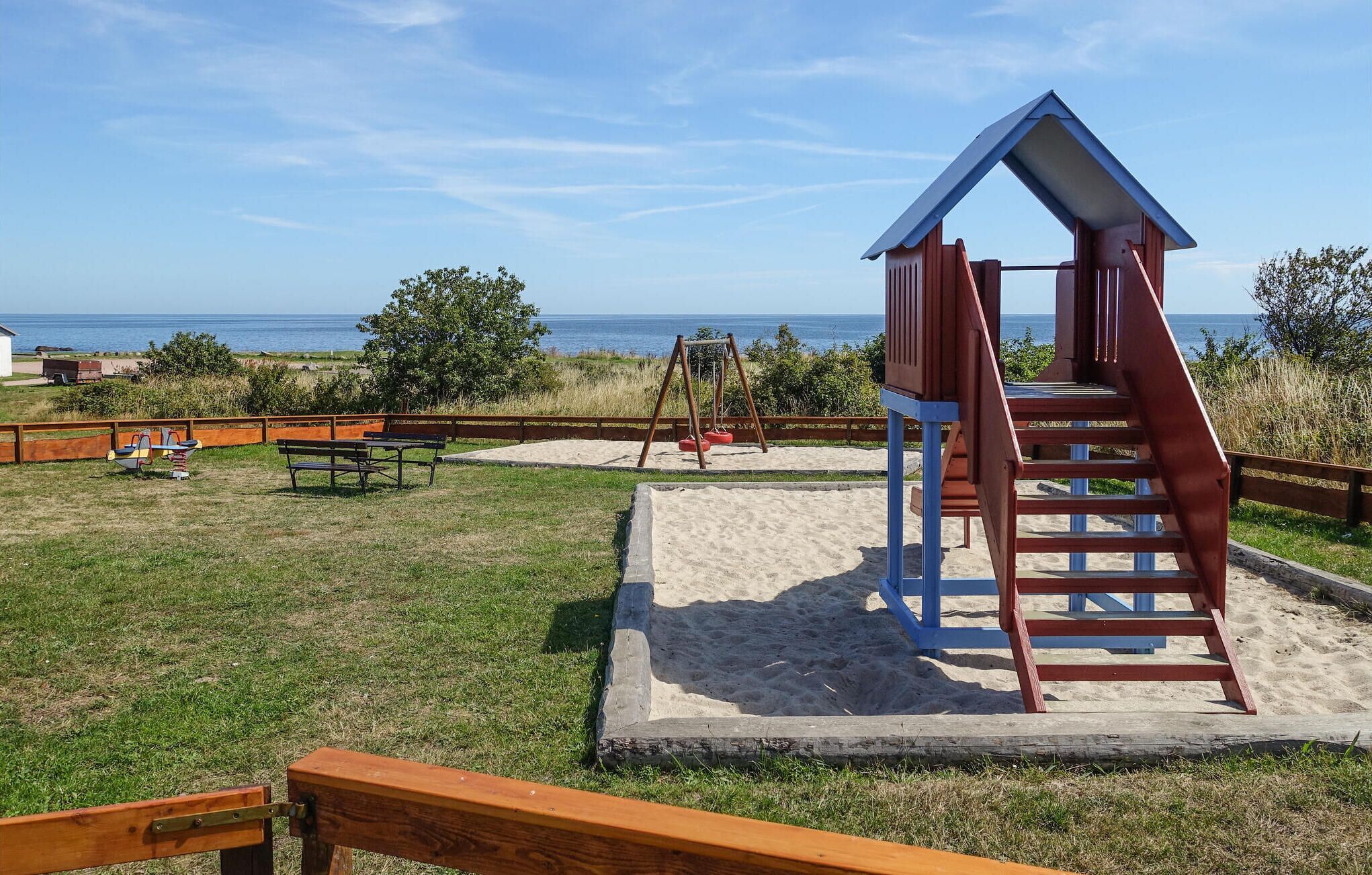 A beachside playground with a slide and swings, surrounded by a wooden fence and a picnic table.
