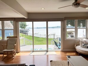 A spacious living room with a large sliding glass door leading to a deck overlooking a body of water.