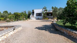 Una villa moderna con entrada de grava, rodeada de vegetación y un cielo azul despejado.