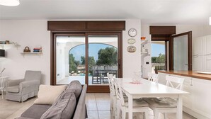 Una sala moderna con sofá, una mesa de comedor con sillas y una zona de cocina. Hay un amplio ventanal corredera que da a un balcón exterior.