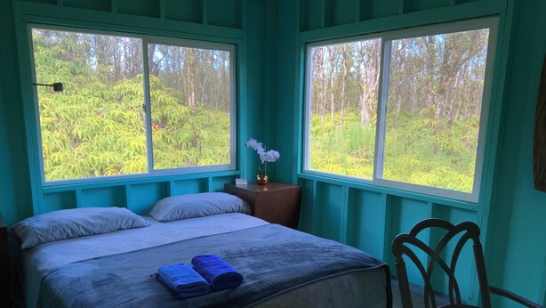 A bedroom with two beds, a nightstand, a chair, and large windows with a forest view.