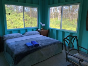 Ein Schlafzimmer mit zwei Betten, einem Nachttisch, einem Sessel und großen Fenstern mit Blick auf einen Wald.