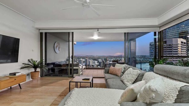 En moderne stue med sofa, sofabord og fjernsyn. Der er en balkon med udsigt over byen.