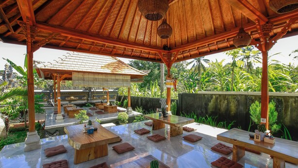 An outdoor seating area with wooden tables and benches, surrounded by lush greenery and a decorative wall. - The Dara Hill (Penida Island)