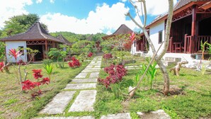A pathway leading to traditional-style buildings surrounded by lush greenery and flowering plants. - The Dara Hill (Penida Island)
