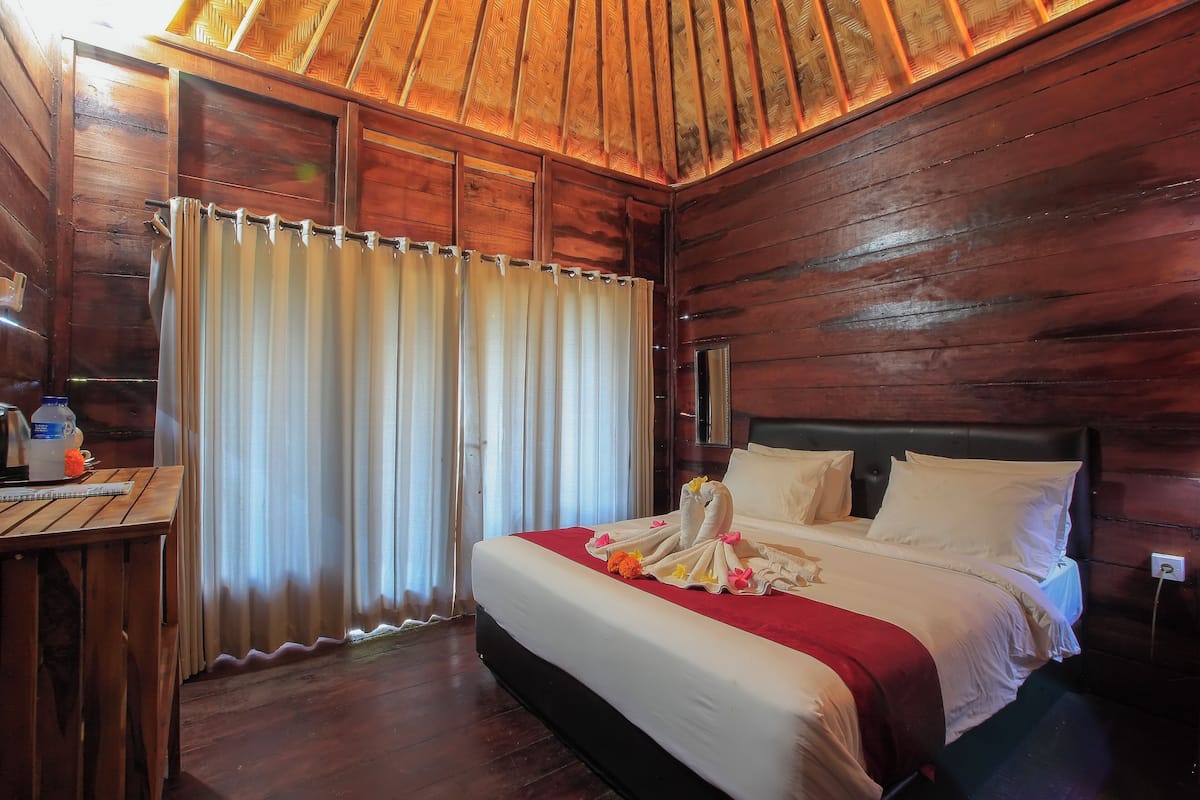 A wooden room with a bed, curtains, and a table with a bottle and a notebook.