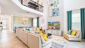 Un vaste salon doté d’un haut plafond, d’un grand ensemble de canapés, d’un coin repas et d’un balcon avec une balustrade.