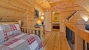 Een gezellige houten blokhut slaapkamer met een bed, een nachtkastje, een lamp en een houten leuning.