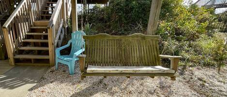 A wooden bench and a blue chair under a wooden pergola, with a staircase leading to an upper level.