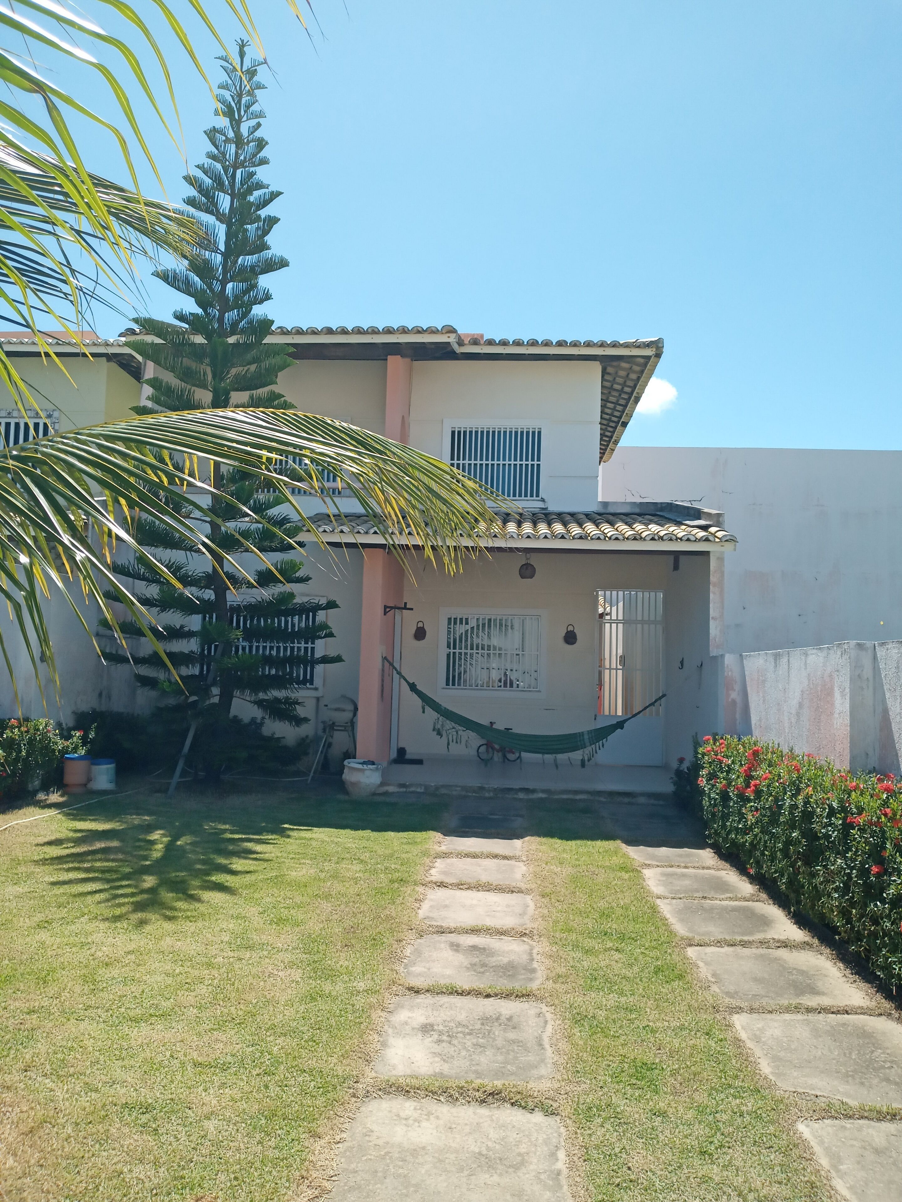 Une maison avec un toit en tuiles, un hamac et un chemin de pierres menant à l’entrée.