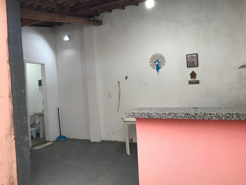 Une pièce avec un mur rose, un comptoir en granit, un balai, une horloge et un petit tableau encadré.