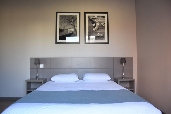 A hotel room with a large bed, two nightstands, and two framed pictures on the wall.