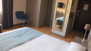 Ein Hotelzimmer mit einem Bett, einem Sessel, einem Schreibtisch, einem Spiegel und einer Tür.