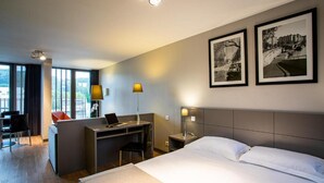 A hotel room with a bed, desk, chair, and two framed pictures on the wall.