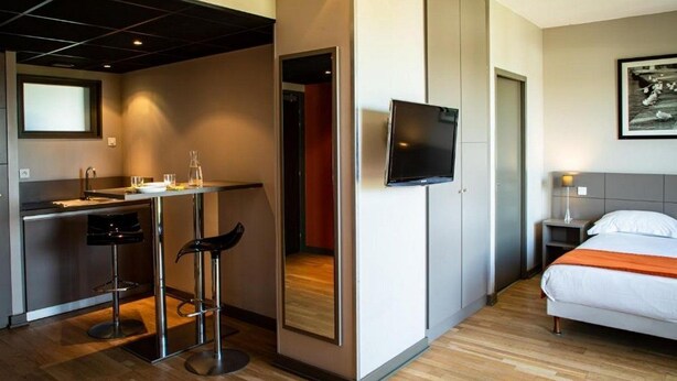 Une chambre d’hôtel compacte comprenant un coin cuisine, un lit, une télévision et un petit espace salon.