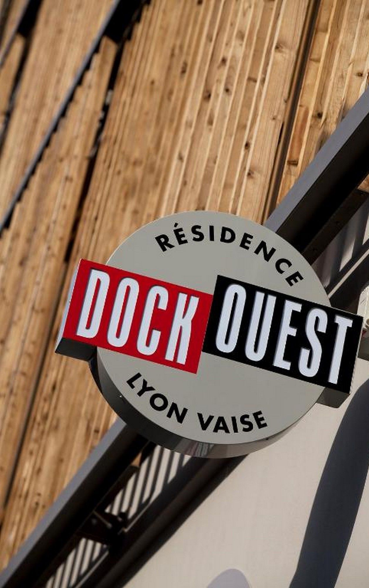 Un panneau circulaire portant l’inscription « Résidence Dock Ouest Lyon Vaisse », indiquant le nom d’un hôtel ou d’une résidence.