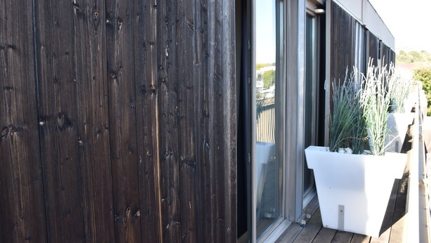 Pared exterior de madera con puerta corredera de vidrio que da a un balcón.