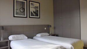 Habitación de hotel con dos camas individuales, un armario grande y dos cuadros en la pared.
