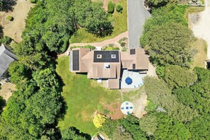 Vue aérienne d’un quartier résidentiel, avec une maison dotée d’un toit équipé de panneaux solaires, d’une piscine et d’un espace patio.