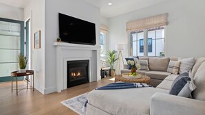 A modern living room with a fireplace, a large flat-screen TV, a sofa, and a coffee table with decorative items. - Modern Luxury Condo In Uptown SB (Santa Barbara)