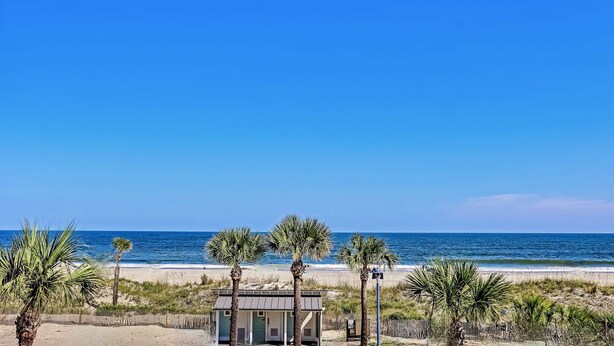 A beach view with a small building, palm trees, and the ocean.