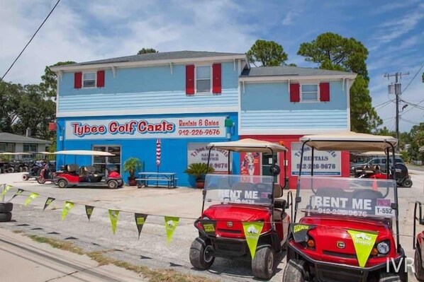 A building with a sign for Tybee Golf Carts Rentals & Sales, featuring two golf carts with 'RENT ME' signs.