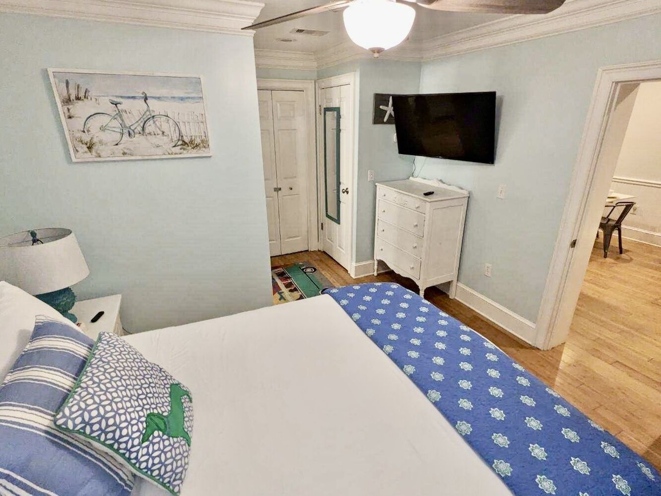 Une chambre à coucher avec un lit, une commode, un téléviseur et un tableau accroché au mur.