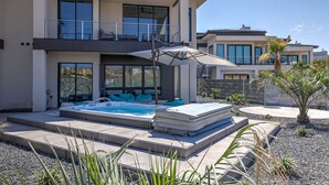 Una casa moderna de dos pisos con jacuzzi, mobiliario exterior y un balcón.
