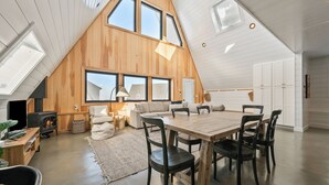 A spacious loft with a high ceiling, large windows, a wooden interior, a dining area, and a built-in fireplace.