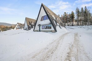 Paisagem coberta de neve com uma casa triangular peculiar, com grandes janelas e uma garagem visível.