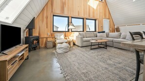 A loft-style living room with a large TV, wooden walls, a fireplace, and a cozy seating area.