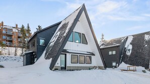 A modern house with a unique triangular roof design, surrounded by snow.