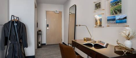 A hotel room with a desk, chair, robe rack, and a large mirror.