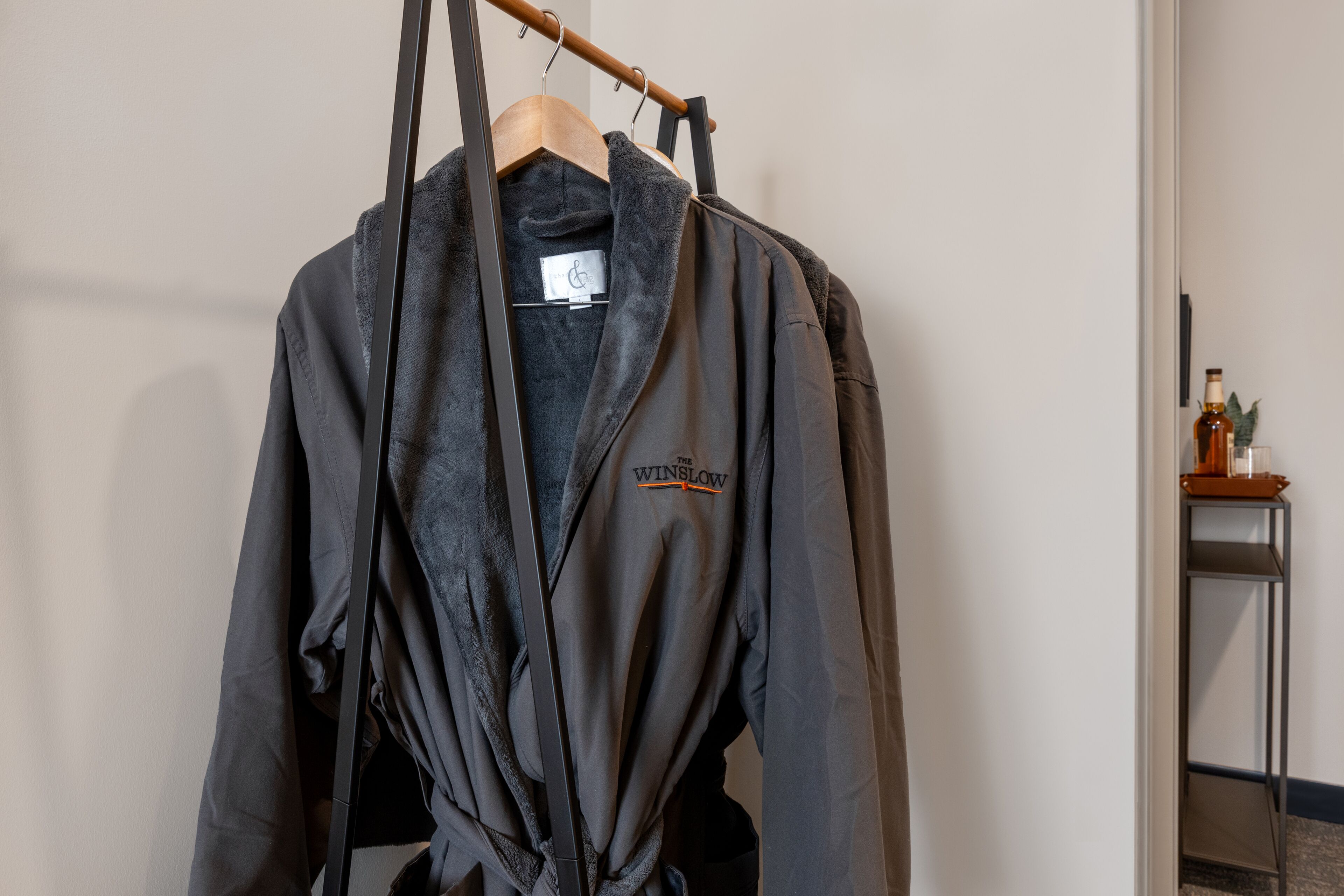 Une robe noire ornée d’un logo, suspendue à un cintre en bois.