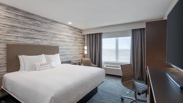 A hotel room with a large bed, a desk, a chair, a TV, and a window with curtains.
