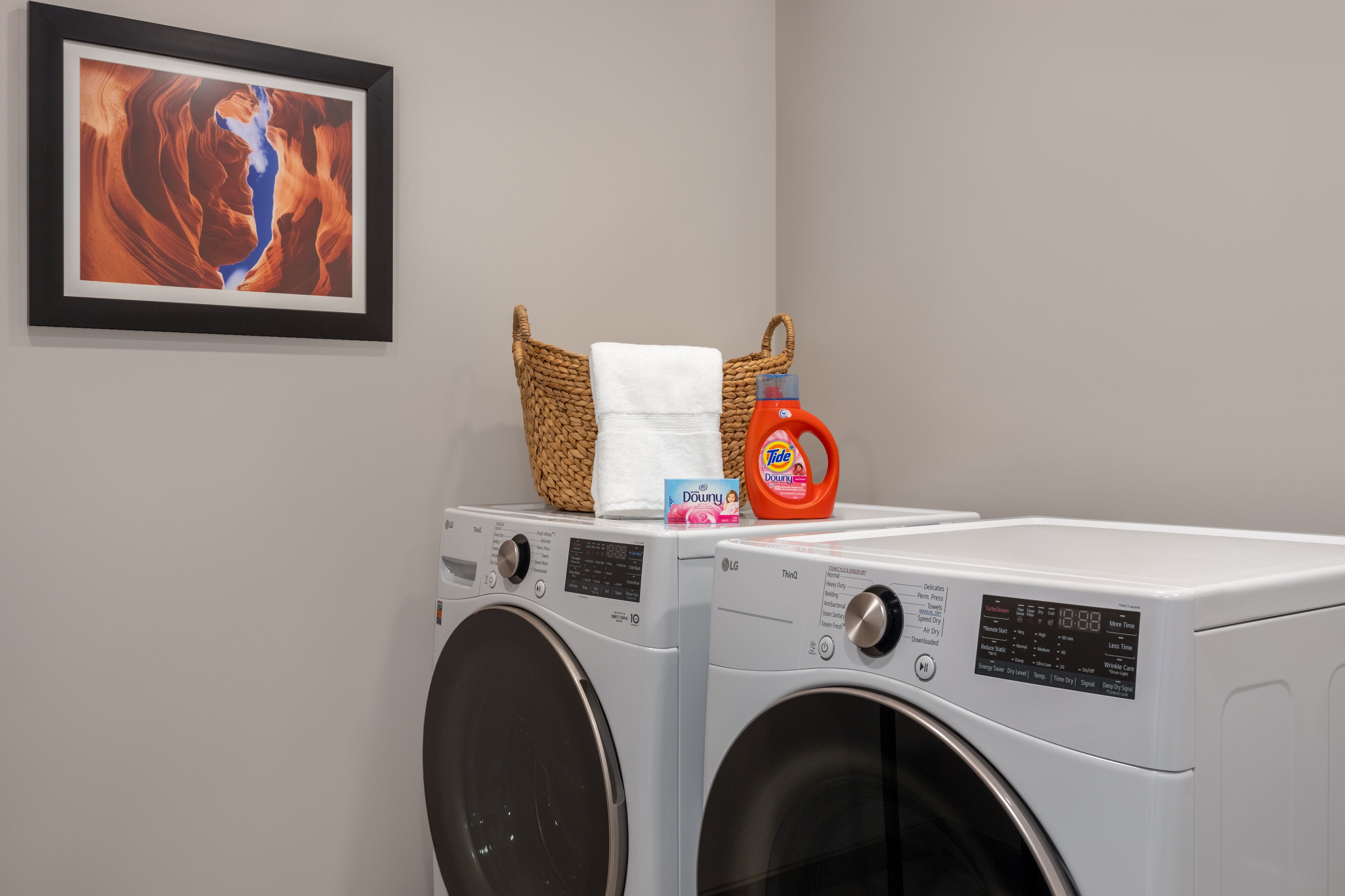 A laundry area with two washing machines, a basket with a towel, and a bottle of laundry detergent.
