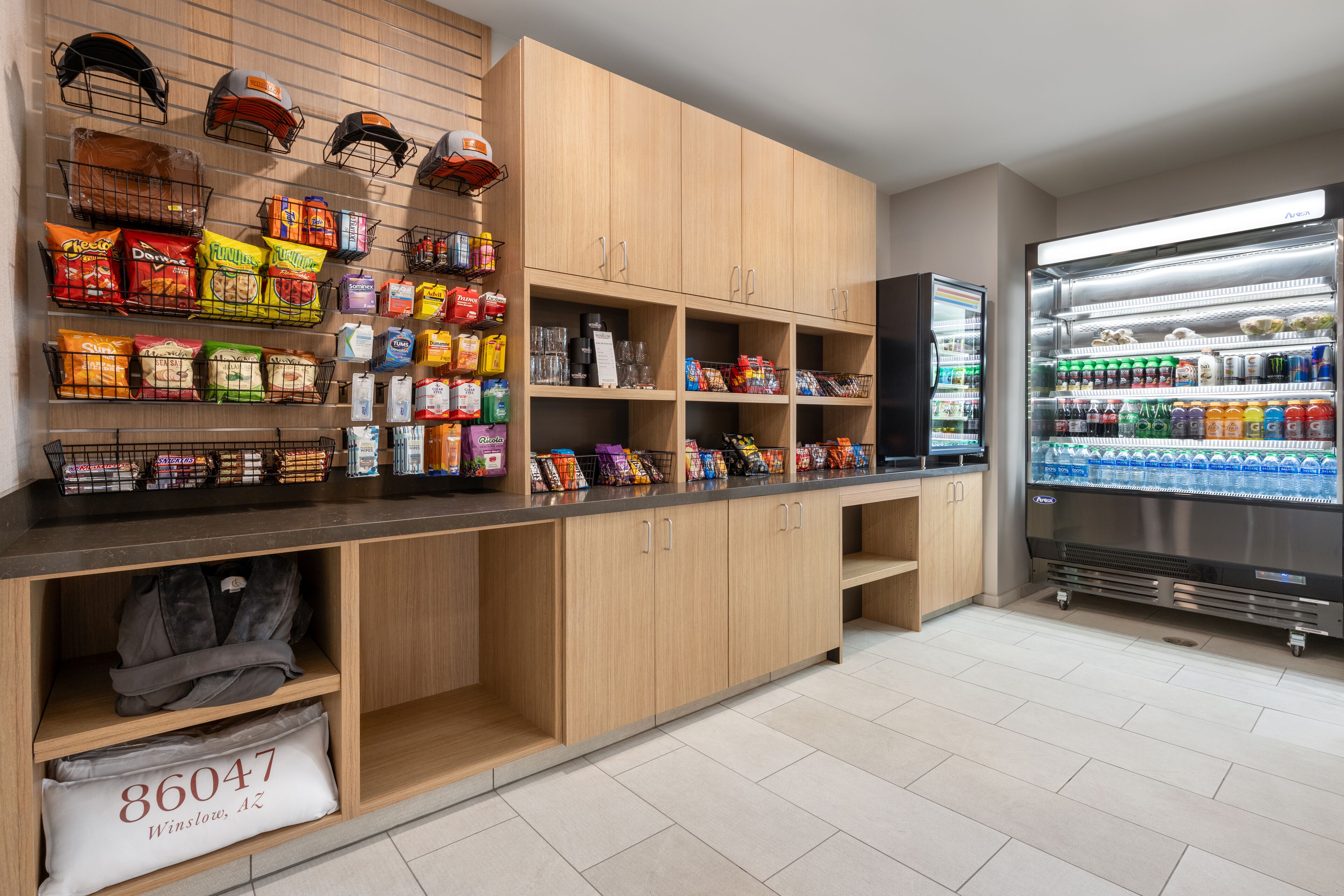 Une petite cuisine propre et moderne, avec des meubles en bois, un plan de travail garni de collations et un réfrigérateur rempli de boissons.