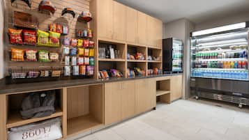 Une petite cuisine propre et moderne, avec des meubles en bois, un plan de travail garni de collations et un réfrigérateur rempli de boissons.