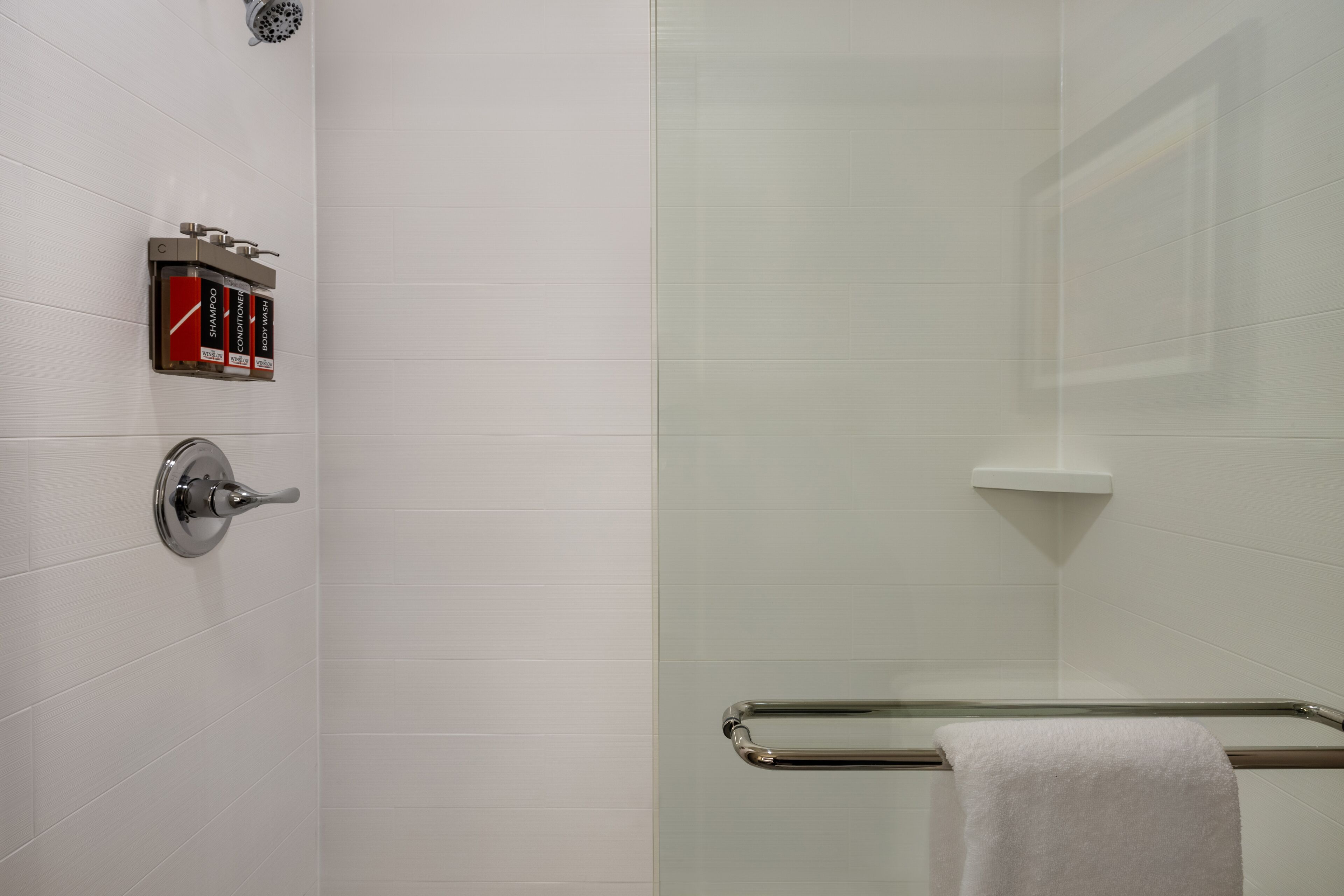 A modern bathroom with white tiled walls, a glass shower enclosure, a towel rack, and a soap dispenser.