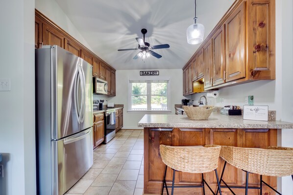 A kitchen with wooden cabinets, a stainless steel refrigerator, a ceiling fan, and a sign indicating a bakery.