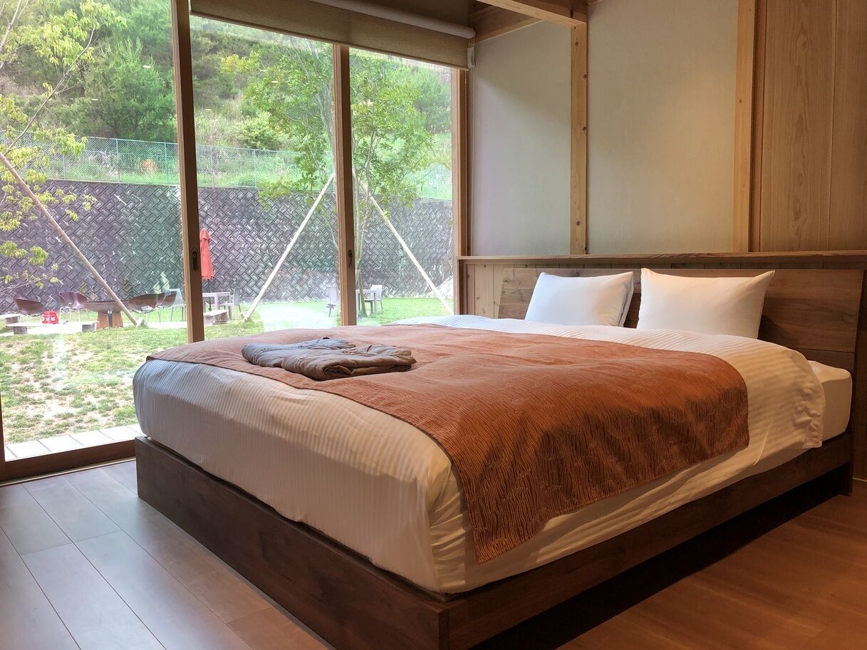 A bedroom with a large bed, wooden headboard, and a view of the outdoors through a large window.